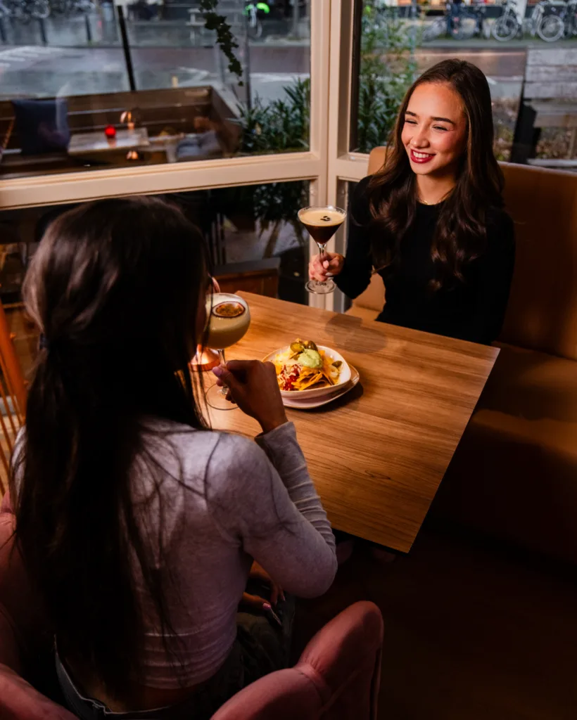 Twee gasten aan tafel bij het raam van Broox Rotterdam, met gerechten en cocktails tijdens het diner