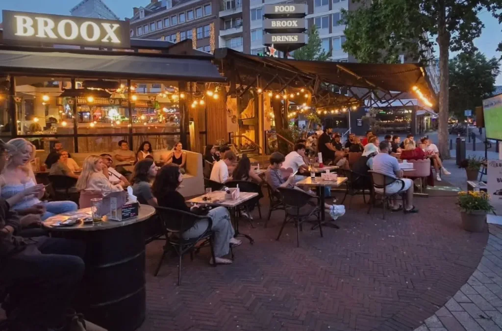 Groepen gasten borrelen op het volle terras van Broox aan de Meent in Rotterdam bij zonsondergang