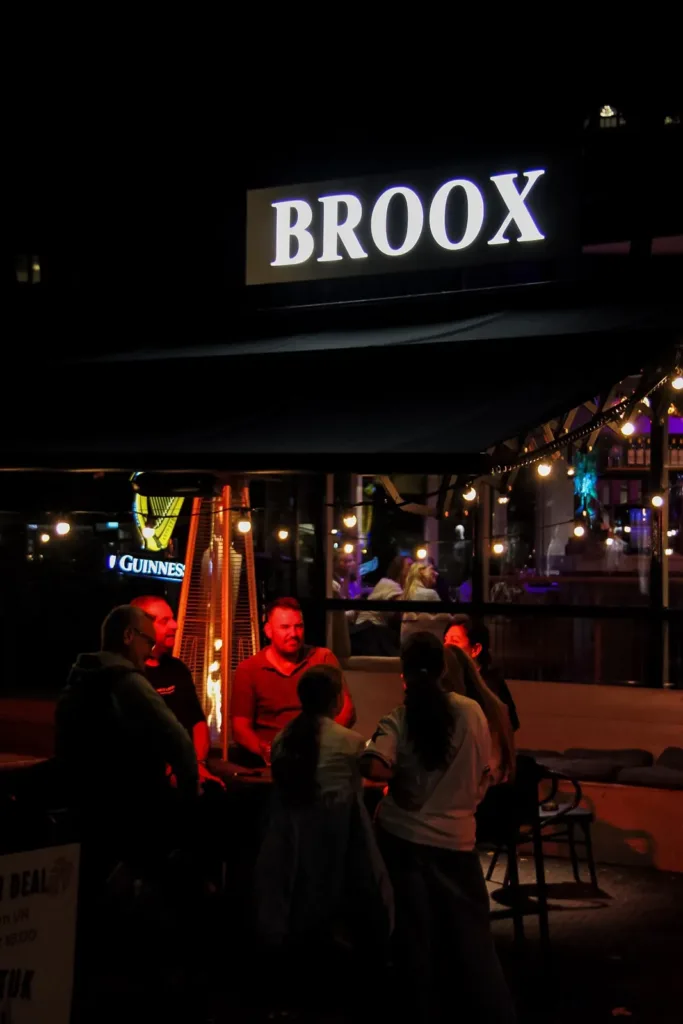 Verlicht BROOX-bord boven het terras met gasten, Broox Rotterdam aan de Meent bij avond