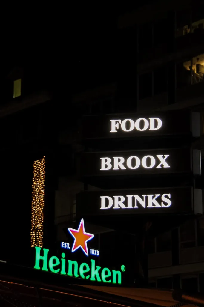 Verlichte borden FOOD, BROOX en DRINKS aan de gevel van Broox Rotterdam aan de Meent bij avond